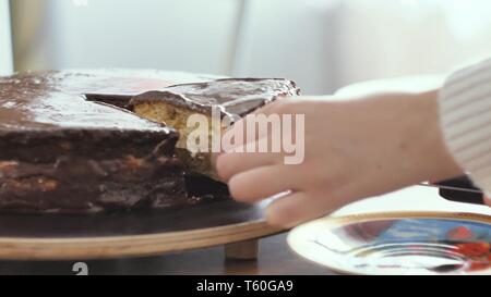 Mädchen schneidet ein Stück Schokolade Kuchen, und legt es auf einen Teller Nahaufnahme Stockfoto