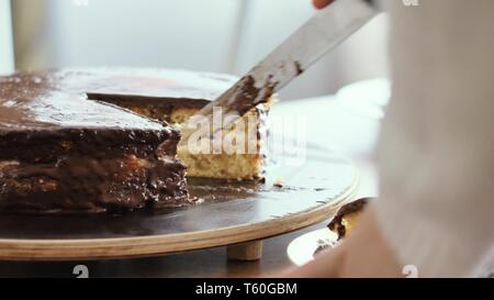 Mädchen schneidet ein Stück Schokolade Kuchen, und legt es auf einen Teller Nahaufnahme Stockfoto