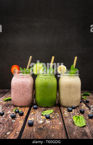 Köstliche bio Banane, Erdbeere, Gurke, Flachs und Chia Saat Frucht Smoothies auf hölzernen Tisch gegen einen schwarzen Schiefer Hintergrund gedreht. Stockfoto