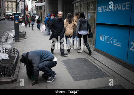 New York City, NY - 06. März 2017: Unbekannter Obdachloser kauert auf der Straße, während andere Fußgänger durch in New York City, NY Pass Stockfoto