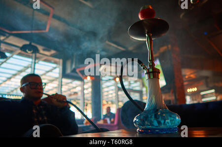 Ein Mann raucht eine Shisha sitzt auf einem Stuhl in einem dunklen Zimmer Stockfoto