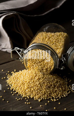 Stapel der goldenen Hirse, glutenfreie Getreide Saatgut, in Glas storage jar auf dunklem Holz Tisch Hintergrund Stockfoto