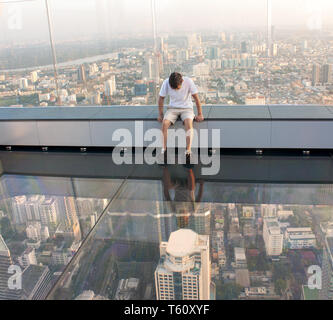 THAILAND, Bangkok - November 25, 2018: ein Mann sitzt auf einem Glasboden, auf dem Dach eines King Power Mahanakhon Gebäude. Derzeit ist es der höchste Bauen Stockfoto