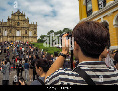 November 2018 - Macao, China: Junge asiatischer Mann mit einer Kamera in einer großen Masse der chinesischen Touristen ein Bild von der Ruinen von St. Paul's zu nehmen Stockfoto