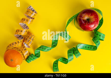 Roter Apfel und Orange mit maßbändern auf gelben Hintergrund. Gewichtsabnahme und schlankheits Behandlungskonzept. Platz für Text Stockfoto