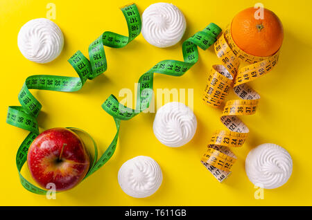 Roter Apfel und Orange mit Maßbändern und Baisers auf gelben Hintergrund. Gewichtsabnahme und schlankheits Behandlungskonzept. Keine Diät Tag Stockfoto