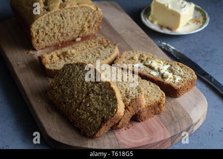 Banana Bread Loaf mit Scheiben und Butter auf Holzbrett auf grauem Hintergrund Stockfoto