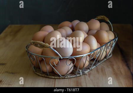 Eier in einem Korb auf rustikalen Holztisch - Kupplung der Eier in der dekorativen Metall Fach Stockfoto