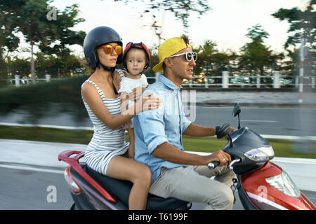 Gerne Paar mit einer kleinen Tochter sind, rot Motorrad auf der Straße an den sonnigen Himmel Hintergrund in Vietnam. Sie legere Kleidung, sunglas Stockfoto