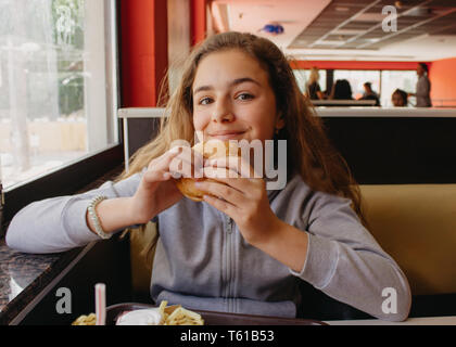 Hübsche, junge Teen Girl mit Appetit essen Hamburger in einem Cafe Stockfoto