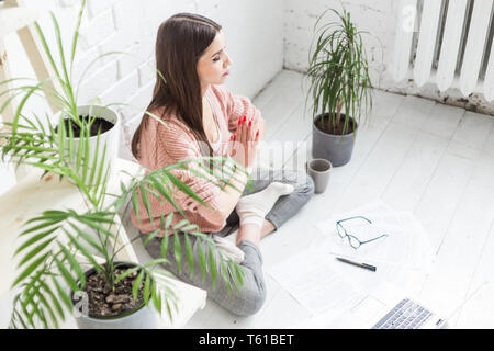 Junge Frau sitzt auf dem Boden in einem Yoga pose in einem hellen Wohnung und arbeitet hinter einem Laptop, einem Freiberufler Mädchen meditiert Stress während der Arbeit. Stockfoto
