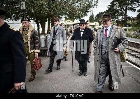 Ein Mann gekleidet als WWII Premierminister Winston Churchill Spaziergänge entlang der Plattform in Winchcombe die von seinen Mitarbeitern während der Kriegszeit flankiert in den Cotswolds Veranstaltung in Gloucestershire Warwickshire Steam Railway. Stockfoto