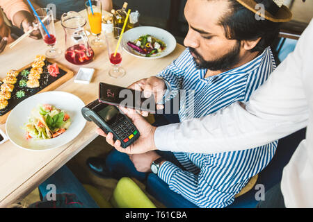 Junge attraktive hinduistischen Mann Bezahlen im Café mit berührungsloser smartphone Zahlung Stockfoto