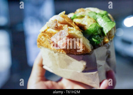 Hand des Menschen nehmen grossen Hamburger, Speck, halten und bereit sind, ihn in seinen Mund zu beißen, bei Thailand foodtruck Ereignis. Stockfoto