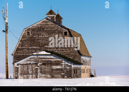 Blue sky over an old, abandoned prairie barn surrounded by snow in Saskatchewan Stockfoto