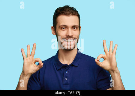 Ein gut aussehender bärtiger Mann in Freizeitkleidung, ok Zeichen gekleidet, mit dem Ausdruck positive Emotion, Gefühl, über blau Hintergrund isoliert. Nahaufnahme portra Stockfoto