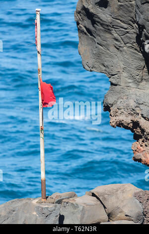 Rote Flagge auf einem Felsen in der Brandung in der Nähe von Playa de Nogales Strand in La Palma, Spanien. Stockfoto