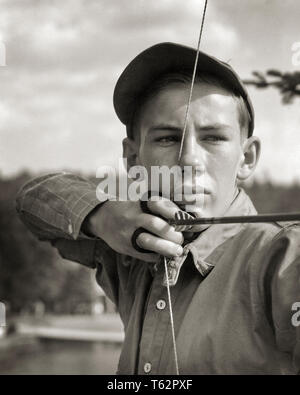 1930er Jahre ernsthafte junge Mann Junge im Summer Camp zeichnen und mit Pfeil und Bogen - Ein 3181 HAR 001 HARS TEENAGER SPIRITUALITÄT VERTRAUEN AUSDRÜCKE B&W ZIELE KOPF UND SCHULTERN ABENTEUER KRAFT UND ERHOLUNG ARCHER an der DISZIPLINIERTEN VERBINDUNG KONZEPTIONELLER CLOSE-UP stilvoll mit dem Ziel, Jugendliche vor - jugendlich PRE-TEEN BOY PRÄZISION ENTSPANNUNG SCHWARZ UND WEISS KAUKASISCHEN ETHNIE KONZENTRATION KONZENTRATION ERMITTLUNG HAR 001 ALTMODISCH ÜBEN Stockfoto