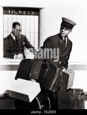 1940 afrikanische amerikanische MANN PORTER TELEFONZENTRALE MIT GEPÄCK IN DER EISENBAHN BAHNHOF - asp x 10845 CAM001 HARS AFRICAN-AMERICAN CAM001 SCHWARZ ETHNIZITÄT ARBEITSMARKT BESCHÄFTIGUNG BERUFE EISENBAHNEN MITARBEITER TICKET COUNTER ATTENDANT Mitte - Mitte - ERWACHSENEN MANN PORTER ROTE KAPPE KOFFER GEPÄCK SCHWARZE UND WEISSE KAUKASISCHEN ETHNIE ARBEITENDEN ALTMODISCHE afrikanische Amerikaner Stockfoto