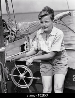 1930er Jahre FRECKLE - KONFRONTIERT JUNGE SITZT AM LENKRAD VON KLEINEN SEGELBOOT - b4215 HAR 001 HARS INSPIRATION MÄNNER SEGEL SOMMERSPROSSEN VERTRAUEN SEGELBOOT TRANSPORT B&W SOMMER REISSVERSCHLUSS ABENTEUER HELM ERHOLUNG SEILE BOOTFAHREN JUGENDLICHE MAST NAVIGIEREN PRE-TEEN PRE-TEEN BOY SEGEL YOUNGSTER SCHWARZ UND WEISS KAUKASISCHEN ETHNIE FRECKLE - KONFRONTIERT HAR 001 ALTMODISCH Stockfoto