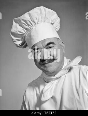 1960er lächelnd MANN CHEF mit SCHNURRBART AUF KAMERA tragen weiße Der TOQUE KÜCHENCHEF HAT HALSTUCH UND BETTWÄSCHE UNIFORM JACKE - c 10524 HAR 001 HARS KOPIE RAUM PERSONEN INSPIRATION MÄNNER BERUF B&W LEINEN AUGENKONTAKT SCHNURRBART SKILL BERUF GLÜCK FÄHIGKEITEN, Kopf und Schultern gut GELAUNT KARRIERE INNOVATION STOLZ HALSTUCH AUTORITÄT BERUFEN LÄCHELT FRÖHLICH kurz um die eigene Kreativität Mitte - Mitte - erwachsenen Mann SOUS-CHEF TOQUE SCHWARZ UND WEISS KAUKASISCHEN ETHNIE CHEF DE CUISINE CHEF LEBENSMITTELZUBEREITUNG HAR 001 ALTMODISCH Stockfoto