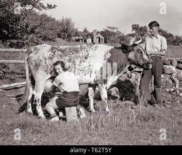 1930er Jahre Lächeln, jugendlich FARM PAAR MÄDCHEN, von der Kamera über die Schulter, melken NORMANDE RASSE DAIRY COW BOY HOLDING KOPF IM FELD - c1362 HAR 001 HARS 1 JUGENDLICHE JUNGE ERWACHSENE TEAMARBEIT FREUDE FREUDE LIFESTYLE ZUFRIEDENHEIT FRAUEN LÄNDLICHE MOLKEREI KOPIE RAUM FREUNDSCHAFT IN VOLLER LÄNGE KUH PERSONEN LANDWIRTSCHAFT MÄNNER PUBERTIERENDE TEENAGER LANDWIRTSCHAFT B&W AUGENKONTAKT WEITWINKEL VIEH FRÖHLICHE CHORE Kühe melken Landwirte wissen STOLZ ÜBER DIE SCHULTER BERUFE LÄCHELT KONZEPTIONELLE MILCHVIEH RASSE FREUDIGE STILVOLLE TEENAGED ZUSAMMENARBEIT JUGENDLICHE SÄUGETIER MITEINANDER junger erwachsener Mann junger Erwachsener FRAU SCHWARZ UND WEISS Stockfoto