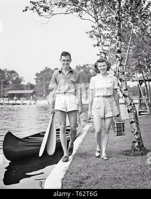 1940 lächelnde junge Paar MANN FRAU ZU FUSS ZUSAMMEN MIT BLICK AUF DIE KAMERA, die Kanu Paddel und PICKNICKKORB LAKESIDE-c 1997 HAR 001 HARS ROMANZE SCHÖNHEIT GEMEINSCHAFT SUBURBAN AUSDRUCK ALTE ZEIT BESETZT NOSTALGIE OLD FASHION 1 Gesichtsbehandlung Stil junger Erwachsener BALANCE SICHERHEIT TEAMWORK URLAUB KANU SPORTLER FREUEN FREUDE LIFESTYLE ZUFRIEDENHEIT FRAUEN VERHEIRATET LÄNDLICHEN EHEPARTNER EHEMÄNNER GESUNDHEIT KOPIE RAUM FREUNDSCHAFT IN VOLLER LÄNGE DAMEN FITNESS PERSONEN MÄNNER ATHLETISCHE VERTRAUEN TRANSPORT AUSDRÜCKE B&W PARTNER AUGENKONTAKT FREIHEIT LAKESIDE ZEIT WEG GLÜCK WELLNESS FRÖHLICHEN ABENTEUER FREIZEIT Stockfoto