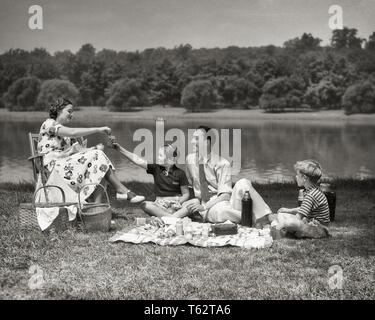 1940 s FAMILIE VON VIER MUTTER VATER TOCHTER SOHN SITZEN AM SEE GENIESSEN FRÜHLING SOMMER Picknick Mittagessen gemeinsam Draußen-c 7776 HAR 001 HARS MANN SEE PAPA VIER REISEN MOM NOSTALGISCHE PAAR 4 SCHÖNHEIT SUBURBAN MÜTTER ALTE ZEIT NOSTALGIE BRUDER OLD FASHION SCHWESTER 1 JUGENDLICHEN TEAMARBEIT SÖHNE GERNE FAMILIEN FREUDE LIFESTYLE FEIER FRAUEN VERHEIRATETE BRÜDER LÄNDLICHEN EHEPARTNER EHEMÄNNER GESUNDHEIT KOPIE RAUM VOLLER LÄNGE DAMEN TÖCHTER PERSONEN INSPIRATION MÄNNER SERENITY GESCHWISTER SPIRITUALITÄT SCHWESTERN VÄTER B&W PARTNER SOMMER GLÜCK FRÖHLICHE FREIZEIT STÄRKE VATIS AUFREGUNG Erholung genießen. Stockfoto