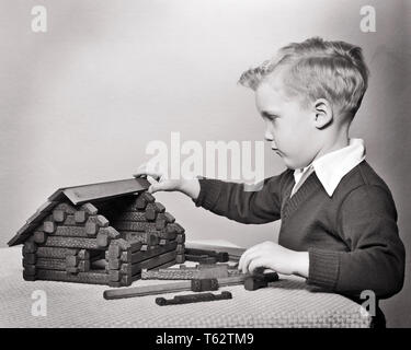 1950 Absicht junge blonde Junge spielt GEBÄUDEMODELL BLOCKHÜTTE MIT LINCOLN ANMELDEN SPIELZEUG SET-j 2683 HAR 001 HARS DISCOVERY PROTOKOLL KENNTNISSE MONTAGE STOLZ KONZEPTIONELLE STILVOLLE LÖSUNG KONSTRUIEREN KREATIVITÄT JUGENDLICHE PRÄZISION SCHWARZ UND WEISS KAUKASISCHEN ETHNIE HAR 001 VORSATZ ALTMODISCH Stockfoto