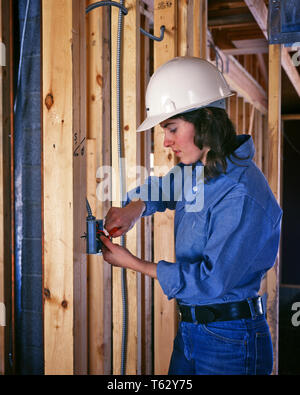 1970er Jahre JUNGE FRAU ELEKTRIKER TRAGEN WEISSE HARD HAT DIE INSTALLATION VON WAND SCHALTERKASTEN IN GEBÄUDE IM BAU-ks 15244 VRE 001 HARS DAMEN PERSONEN INSPIRATION BERUF HANDWERK VERTRAUEN DENIM BRUNETTE BLUE COLLAR SKILL BERUF FÄHIGKEITEN HARTEN HUT KARRIERE ARBEITSRECHTE IN GELEGENHEIT BESCHÄFTIGUNG BERUFE VERBINDUNG FRAMING OUTLET MITARBEITER BEFREIUNG HANDEL HANDWERK ELEKTRIKER GLEICHSTELLUNG VON FRAUEN IM AUFBAU junger Erwachsener FRAU KAUKASISCHEN ETHNIE INSTALLATION ARBEITENDEN ALTMODISCH Stockfoto