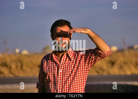 1980 s MANN SCHATTIERUNG AUGEN AUS SONNENLICHT MIT HAND tragen rot und weiß kariertes Hemd STEHEN AUF BEACH-ks 18007 BLE 001 HARS MENSCHEN MÄNNER GELEGENHEIT SEHEN SONNENAUFGANG BEOBACHTEN WAHRNEHMUNG BLICK STILVOLLE VISTA ZUSAMMENARBEIT BEOBACHTUNG SCHATTIERUNG junger erwachsener Mann KAUKASISCHEN ETHNIE ALTMODISCH Stockfoto