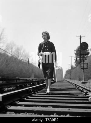 1950er Jahre 1960er Jahre unglückliche Frau WANDERN AUF BAHNGLEISE BEI KOFFER-s10038 DEB001 HARS RAILROAD PASSEN LIFESTYLE LÄNDLICHEN GROWNUP HOME LEBEN KOPIEREN RAUM VOLLER LÄNGE PERSONEN GROWN-UP B&W TRAURIGKEIT TITEL EINZELNE FIGUR FREIHEIT RUNAWAY AEROBE KONZEPTIONELLE GUTE GESUNDHEIT VERPASST ESCAPE DEB001 Mitte - Mitte - ERWACHSENE FRAU MENSCHEN ERWACHSENE SCHWARZ UND WEISS KAUKASISCHEN ETHNIE ALTMODISCH Stockfoto