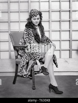 1930 1940 s FRAU MIT LEOPARD HAUT Hut und Mantel mit PELZBESATZ, die versuchen, auf ein paar HIGH HEELS sitzen im Stuhl - s 7325 HAR 001 HARS KOPIE RAUM IN VOLLER LÄNGE mit halber Länge DAMEN PERSONEN HAUT B&W SHOPPER BRUNETTE SHOPPER ENTDECKUNG STILE UND VERSUCHEN DIE VERKLEIDUNG VERFOLGTE PELT STILVOLLE LEOPARD HAUT AUF, die versuchen, auf MODE PELZE SCHMERZHAFT JUNGEN ERWACHSENEN FRAU SCHWARZ UND WEISS KAUKASISCHEN ETHNIE HAR 001 ALTMODISCH wunde Füße Stockfoto