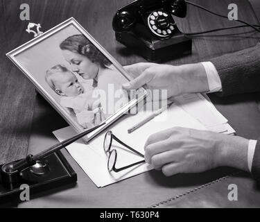 Der 1940er ist Geschäftsmann, Hände halten ein GERAHMTES FOTO VON SEINER FRAU UND BABY AUF SEINEM SCHREIBTISCH MIT TELEFON PEN PAPIER UND BRILLEN-s9495 HAR 001 HARS PAAR MÜTTER ALTE ZEIT NOSTALGIE OLD FASHION 1 FOTO JUGENDLICHE JUNGE ERWACHSENE FAMILIEN FREUDE LIFESTYLE ZUFRIEDENHEIT FRAUEN GEHEIRATET STUDIO SHOT EHEPARTNER EHEMÄNNER LEBEN ZU HAUSE KOPIEREN PLATZ DAMEN PERSONEN PFLEGE MÄNNER BRILLEN B&W PARTNER HOHEN WINKEL SEIN UND STOLZ EINEN DER AUF BERUFE konzeptionellen Rahmen jugendliche Mitte - Mitte - erwachsenen Mann MAMMEN ZWEISAMKEIT FRAUEN JUNGE ERWACHSENE FRAU BABY GIRL SCHWARZ UND WEISS KAUKASISCHEN ETHNIE HÄNDE NUR HAR 001 ALTMODISCH Stockfoto