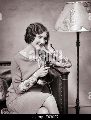 1920er lächelnd gut gekleidete Frau mit LEUCHTER TELEFON-t 2306 HAR 001 HARS HALBE LÄNGE DAMEN PERSONEN B&W LEUCHTER BRUNETTE ZIEMLICH GLÜCK FRÖHLICH STILE FRISUR LAMPENSCHIRM TELEFONE LÄCHELT FINGER WELLEN VERBINDUNG STEHLEUCHTE TELEFONE FREUDIGE STILVOLLE MODE JUNGE ERWACHSENE FRAU SCHWARZ UND WEISS KAUKASISCHEN ETHNIE HAR 001 ALTMODISCH Stockfoto