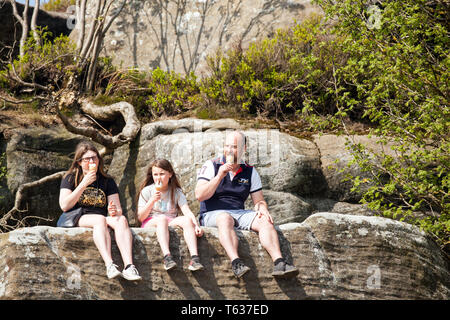 Familie sitzt auf Felsen genießen Eis essen Kornett in der frühlingssonne an Brimham Rocks Nidderdale in den Yorkshire Dales England Großbritannien Stockfoto