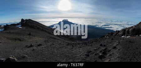 Panoramablick auf den Mawenzi Peak von Stella Point in der Nähe der Gipfel des Mount Kilimanjaro. Mawenzi steigt über den Wolken unter hellen Morgen Sonne. Stockfoto