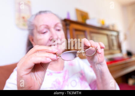 Eine alte Frau setzt auf ihre Brille Stockfoto