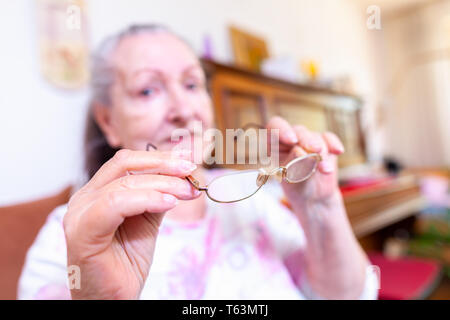 Eine alte Frau setzt auf ihre Brille Stockfoto