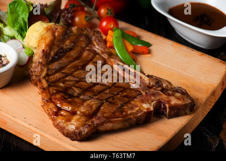 Gegrilltes große T-Bone Steak garniert mit Kräutern, Tomaten und Salz Stockfoto