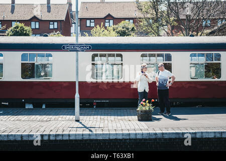 Sheringham, Großbritannien - 21 April, 2019: Zwei Menschen stehen auf einem Bahnsteig in Sheringham, die Poppy Linie Zug, ein Erbe Steam Railway, der von S Stockfoto