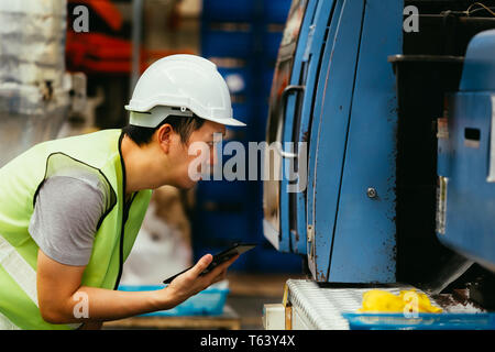 Jungen asiatischen Männlich schwere industrielle Arbeiter in Arbeitskleidung einheitliche Überwachung und Qualitätskontrolle mit einem Tablet Maschinen in der Fertigung zu prüfen. Stockfoto
