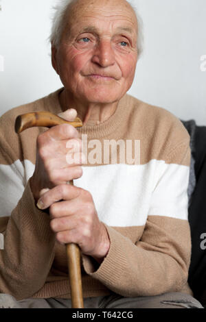 Porträt eines lächelnden alten Mann, der seine Hände auf den Griff eines hölzernen Spazierstock, Gesundheit zu Hause. Stockfoto