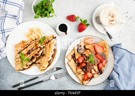 Crepes oder Blini mit Banane, Erdbeer und Schokolade, Kaffee und Dekoration von minzeblatt und Schokoladensauce. Ansicht von oben, flach Komposition legen Stockfoto