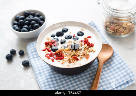 Schüssel Joghurt mit Müsli, Goji Beeren und Heidelbeeren auf ein Blau kariertes Textil. Gesundes Frühstück essen Stockfoto