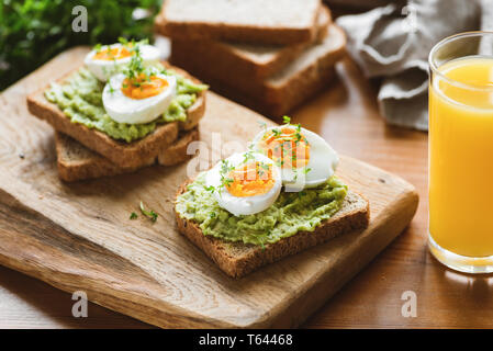 Toast mit Avocado, Ei, micro Grüns und Glas Orangensaft auf hölzernen Tisch. Gesunde nützliche Frühstück Stockfoto