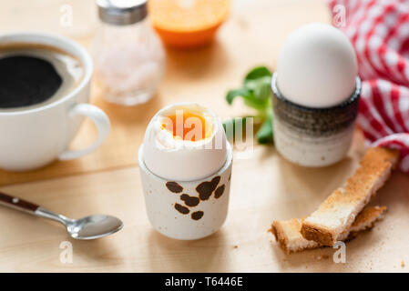 Weich gekochte Eier und Toast Frühstück mit einer Tasse schwarzen Kaffee am Tisch serviert Stockfoto