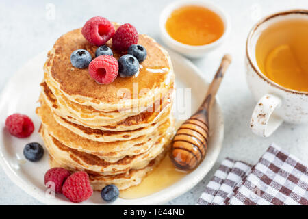 Hausgemachte Pfannkuchen mit Beeren und Honig mit Tasse grünen Tee mit Zitrone serviert. Detailansicht. Leckeres Frühstück essen Stockfoto