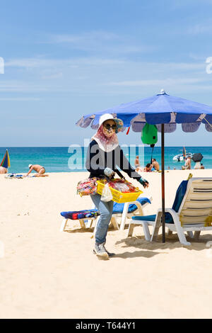 Phuket, Thailand, 20. Februar 2018: Eine weibliche Verkäuferin mit einem Tablett entlang Karon Beach. Stockfoto