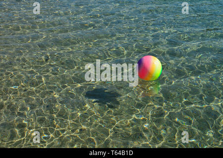 Strand Erholung Konzept, bunten beach ball schwimmt auf der Oberfläche von klaren, transparenten Meer Wasser, Menge funkelt, Fisch-förmigen Schatten, Kopieren s Stockfoto